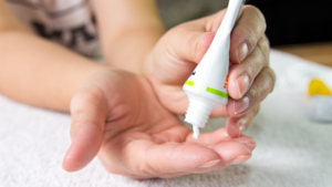 Różne tubki maści z witaminą F ułożone na stole z zielonymi liśćmi w tle.