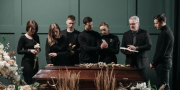 Zasiłek pogrzebowy 2024: Co warto wiedzieć? Wiadomości Drewniana trumna otoczona białymi kwiatami, symbolizująca koszty i organizację pogrzebu.